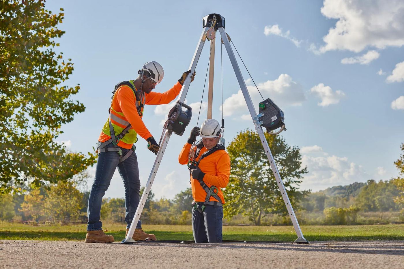 Two workers setting a rescue tripod over a manway