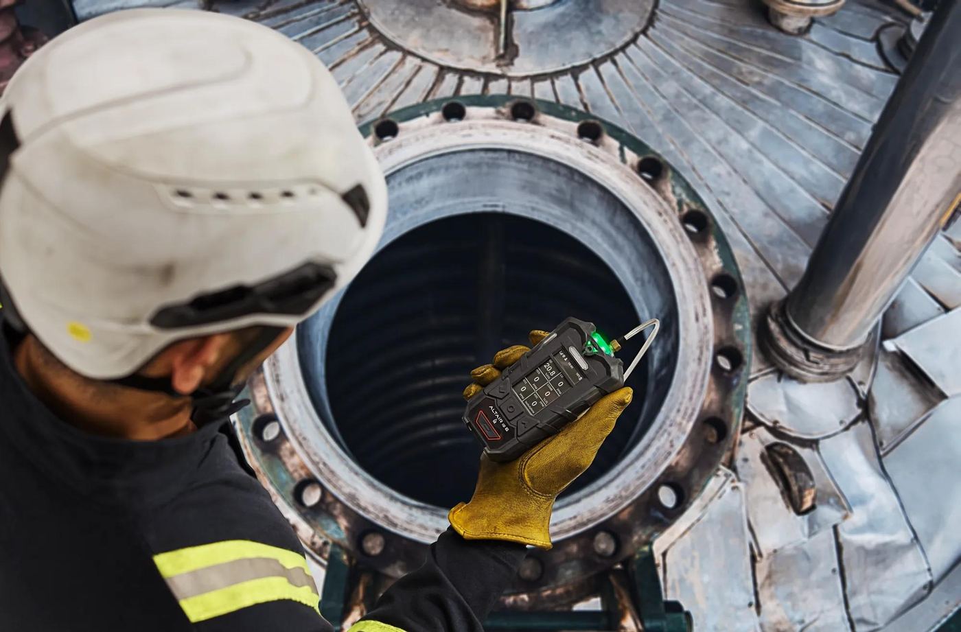 Worker lowering a gas detector into the manway of a vessel before entry